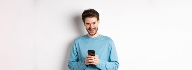 Imagem de homem bonito usando smartphone e rindo sorrindo para a câmera alegre em pé sobre as costas brancas