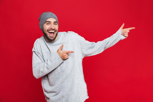 Imagem de homem caucasiano de 30 anos com a barba por fazer rindo e apontando o dedo para o lado isolado