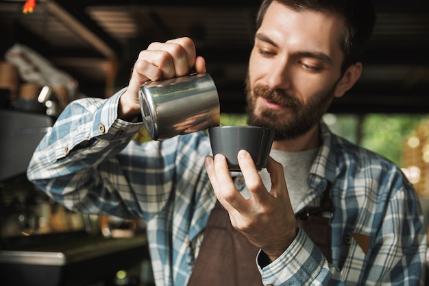 Imagem de homem moreno barista usando avental fazendo café enquanto trabalhava em um café ou cafeteria ao ar livre