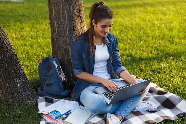 Imagem de incrível estudante jovem bonita no parque usando o computador portátil.
