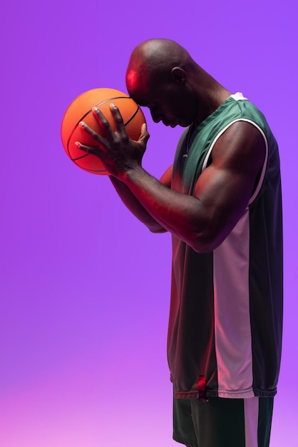 Foto imagem de jogador de basquete afro-americano com basquete em fundo roxo neon. conceito de esportes e competição.