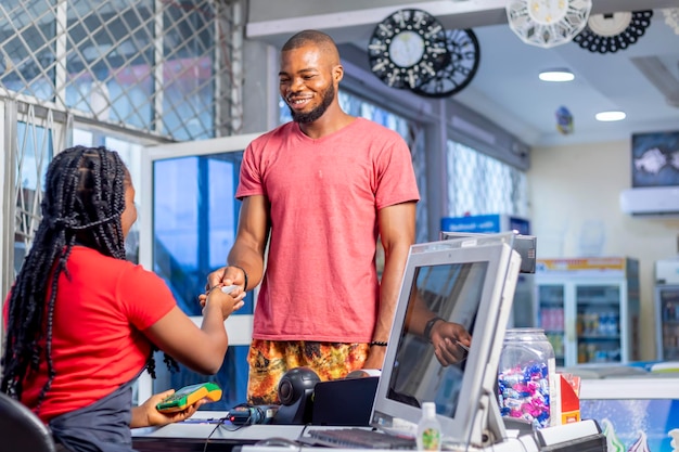 Imagem de jovem africano dá cartão de crédito a caixa no espaço de trabalho no supermercado