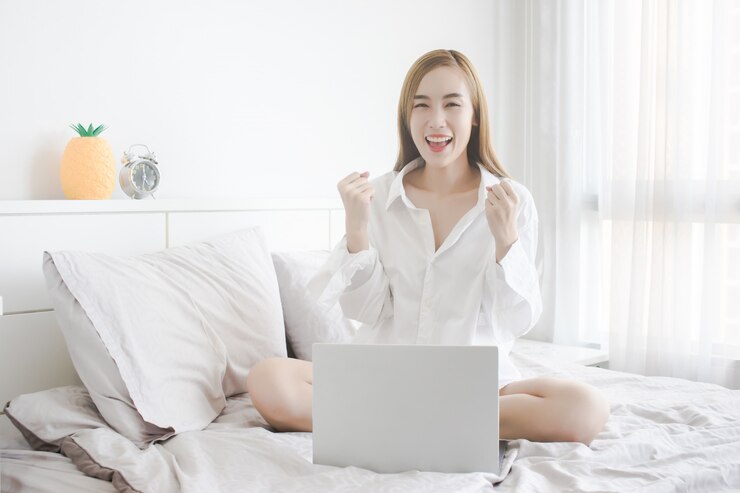Imagem de jovem alegre sentado na cama e usando o computador portátil
