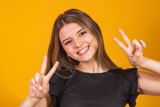 Imagem de jovem feliz isolado sobre fundo amarelo, mostrando um gesto de paz. câmera olhando.