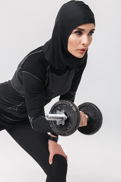 Imagem de jovem mulher fitness muçulmano posando isolado fazer exercícios com halteres.