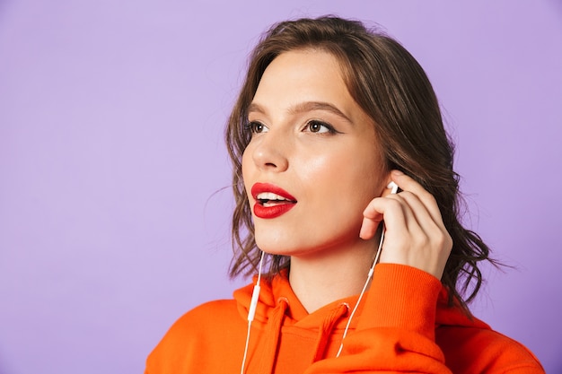 Imagem de jovem posando isolado sobre a parede roxa ouvindo música com fones de ouvido.