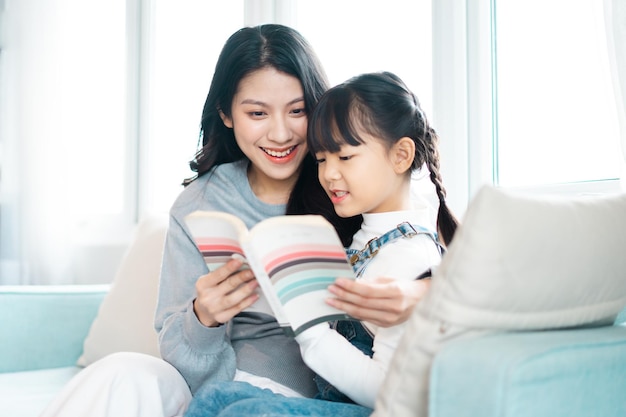 Imagem de mãe e filha sentadas no sofá lendo um livro