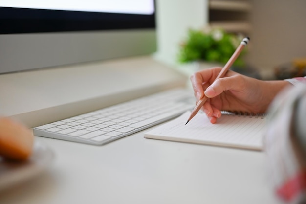 Foto imagem de mãos fechadas uma mulher escrevendo algo em seu caderno na mesa do computador