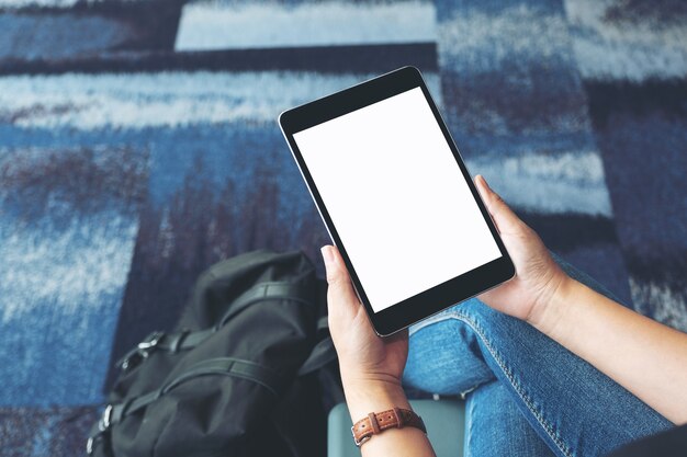 Imagem de maquete das mãos de uma mulher segurando e usando um tablet pc preto com tela em branco enquanto está sentada no aeroporto