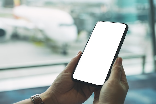 Imagem de maquete das mãos de uma mulher segurando e usando um telefone celular preto com tela em branco enquanto está sentada no aeroporto