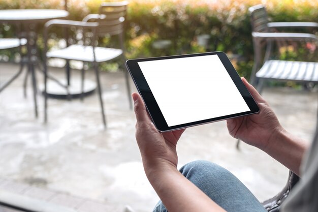 Imagem de maquete de mãos de mulher segurando preto tablet pc com tela branca de mesa em branco no café