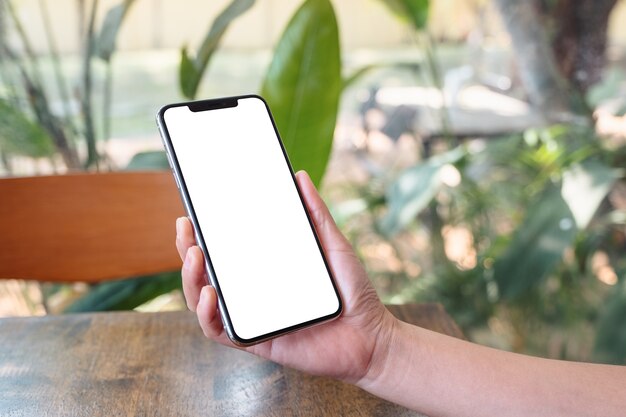 Imagem de maquete de mãos segurando um telefone celular preto com tela em branco e fundo verde da natureza