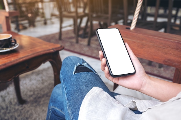 Imagem de maquete de mãos segurando um telefone celular preto com uma tela em branco enquanto está sentado no café