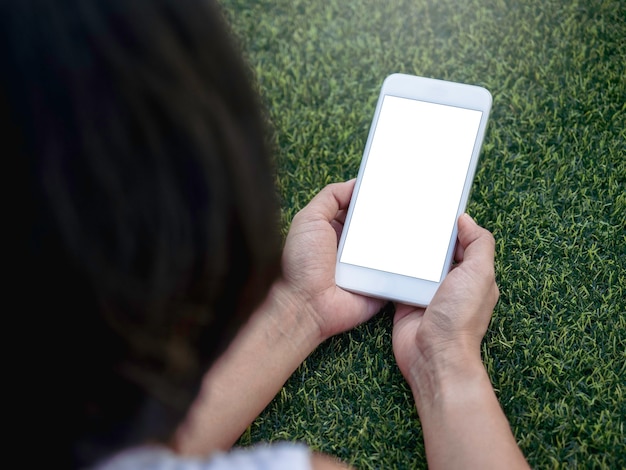 Imagem de maquete de telefone. Tela em branco branca no celular nas mãos da mulher no fundo verde da grama artificial. Mão segurando um smartphone branco com tela vazia.