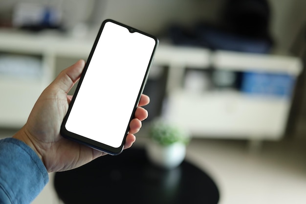 Imagem de maquete de um homem segurando o celular preto com tela branca em branco na sala de estar em casa