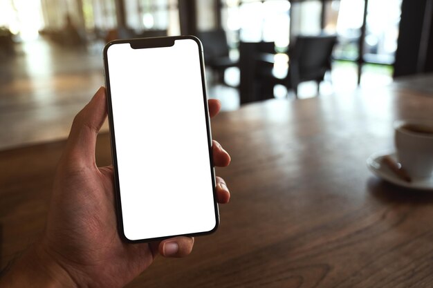 Imagem de maquete de um homem segurando o celular preto com tela branca em branco no café