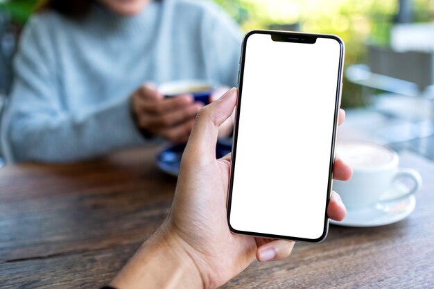 Imagem de maquete de um homem segurando um telefone celular preto com uma tela em branco e uma mulher tomando café em um café