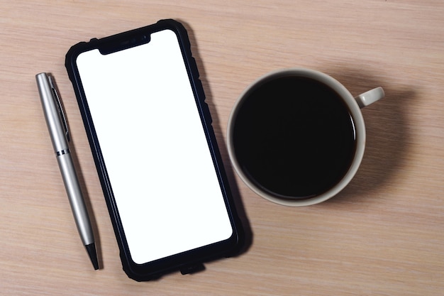 Imagem de maquete de um smartphone com a tela em branco, caneta e uma xícara de café em uma mesa de madeira.
