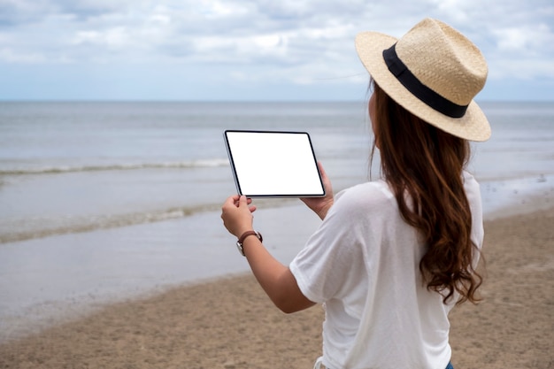 Imagem de maquete de um woamn segurando um tablet pc preto com uma tela em branco à beira-mar