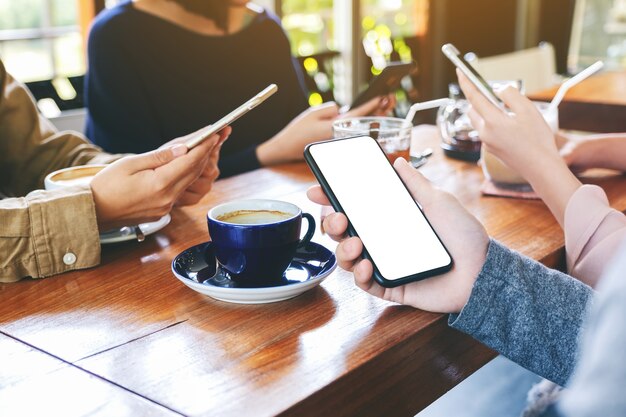 Imagem de maquete de uma mão segurando e usando um celular preto com uma tela em branco com amigos em um café