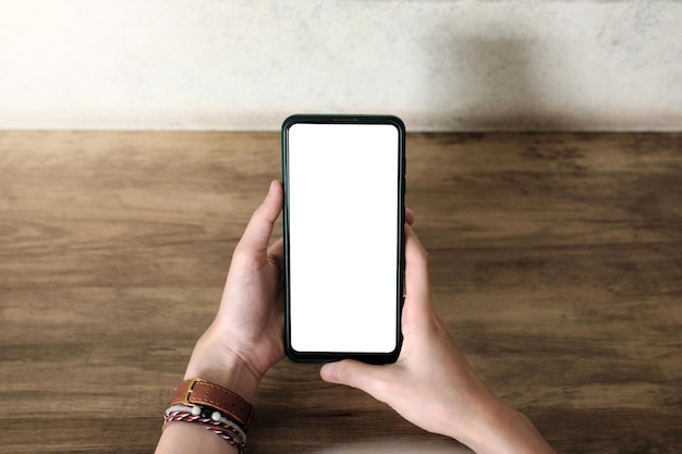 Imagem de maquete de uma mão segurando o celular com tela em branco na mesa de madeira