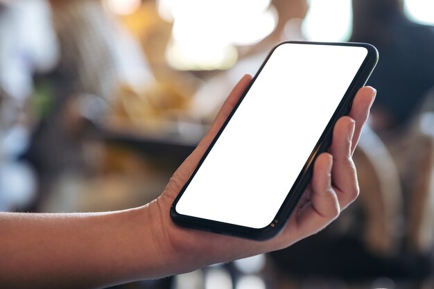 Imagem de maquete de uma mão segurando um celular preto com uma tela em branco em um café