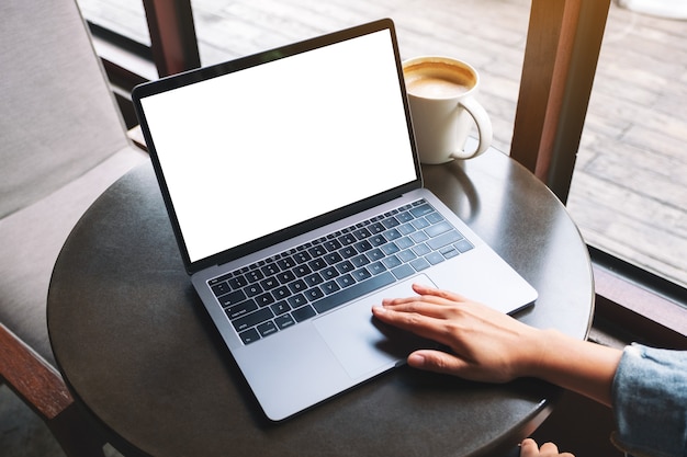 Imagem de maquete de uma mão usando e tocando no touchpad do laptop com tela de desktop em branco e xícara de café na mesa