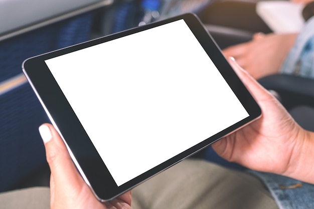 Imagem de maquete de uma mulher segurando e olhando para um tablet pc preto com uma tela de desktop em branco enquanto está sentado na cabine