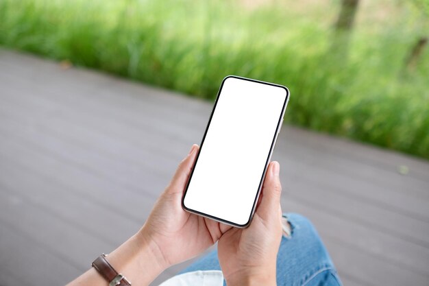 Imagem de maquete de uma mulher segurando o celular com tela branca em branco do desktop ao ar livre