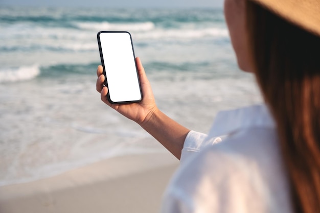 Imagem de maquete de uma mulher segurando o celular com tela em branco na praia