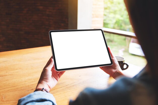 Imagem de maquete de uma mulher segurando o tablet digital com tela branca em branco do desktop no café