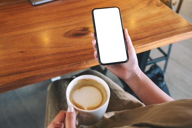 Imagem de maquete de uma mulher segurando um celular preto com uma tela em branco enquanto bebe café