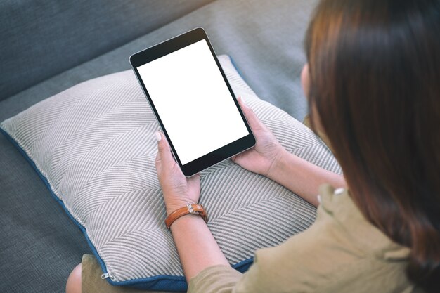 Imagem de maquete de uma mulher segurando um tablet pc preto com uma tela de desktop em branco enquanto está sentada na sala de estar sentindo-se relaxada
