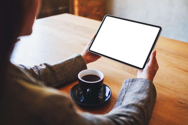 Imagem de maquete de uma mulher segurando um tablet pc preto com uma tela em branco e uma xícara de café em cima da mesa