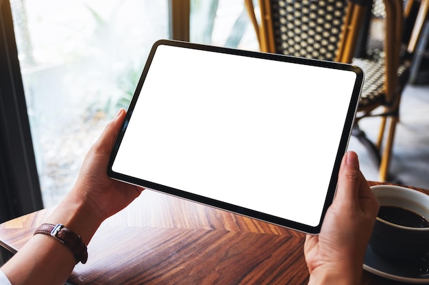 Imagem de maquete de uma mulher segurando um tablet pc preto com uma tela em branco e uma xícara de café em cima da mesa