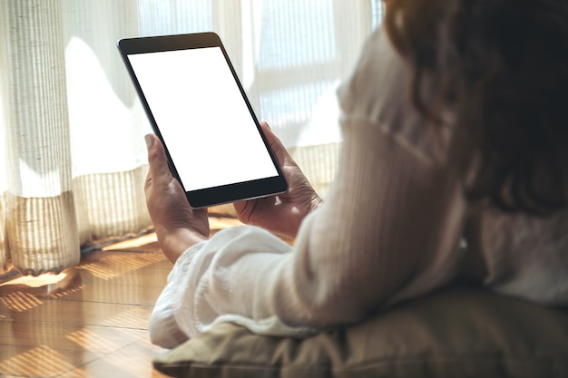 Imagem de maquete de uma mulher segurando um tablet pc preto com uma tela em branco enquanto está deitada no chão sentindo-se relaxada