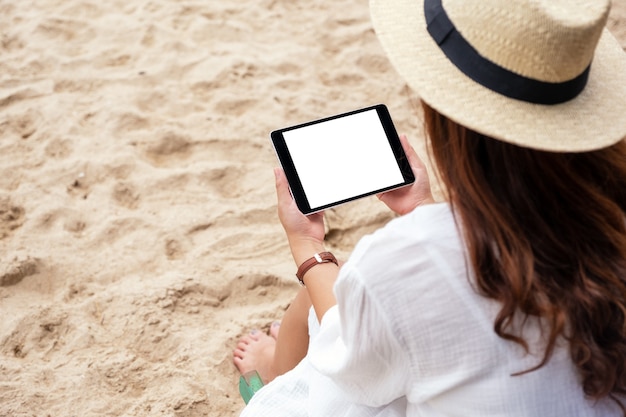 Imagem de maquete de uma mulher segurando um tablet pc preto com uma tela em branco, enquanto está sentada em uma cadeira de praia