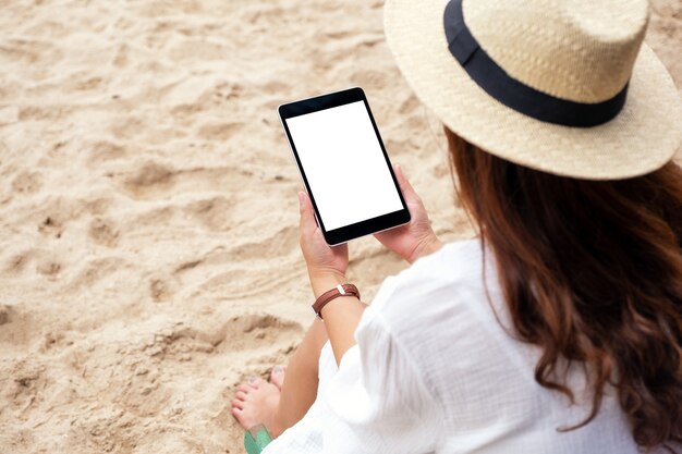 Imagem de maquete de uma mulher segurando um tablet pc preto com uma tela em branco, enquanto está sentada em uma cadeira de praia