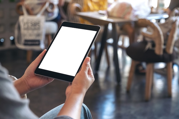 Imagem de maquete de uma mulher segurando um tablet pc preto com uma tela em branco enquanto está sentado em um café