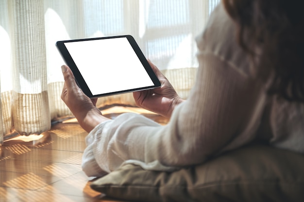 Imagem de maquete de uma mulher segurando um tablet pc preto com uma tela em branco na área de trabalho horizontalmente enquanto se deita no chão e se sente relaxada