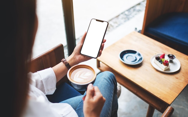 Imagem de maquete de uma mulher segurando um telefone celular com uma tela em branco enquanto toma café no café