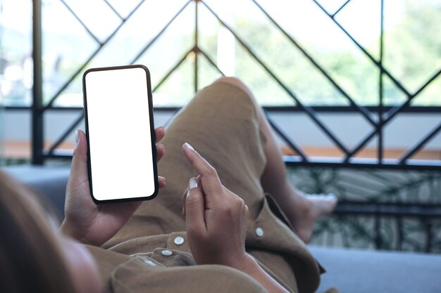 Imagem de maquete de uma mulher segurando um telefone celular preto com uma tela em branco enquanto deitada na sala de estar sentindo-se relaxada