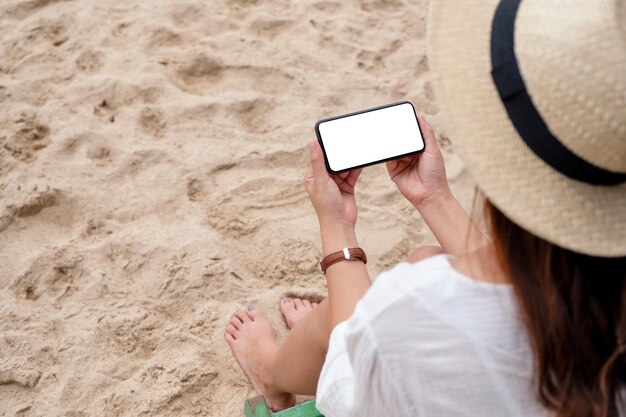 Imagem de maquete de uma mulher segurando um telefone celular preto com uma tela em branco, enquanto está sentada em uma cadeira de praia