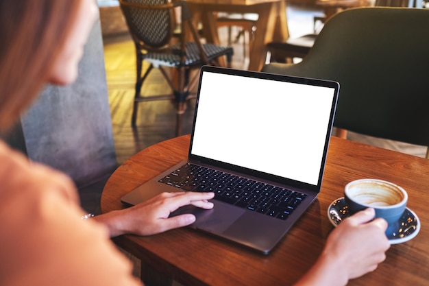 Imagem de maquete de uma mulher tocando no touchpad do computador portátil com tela branca em branco do desktop enquanto bebe café