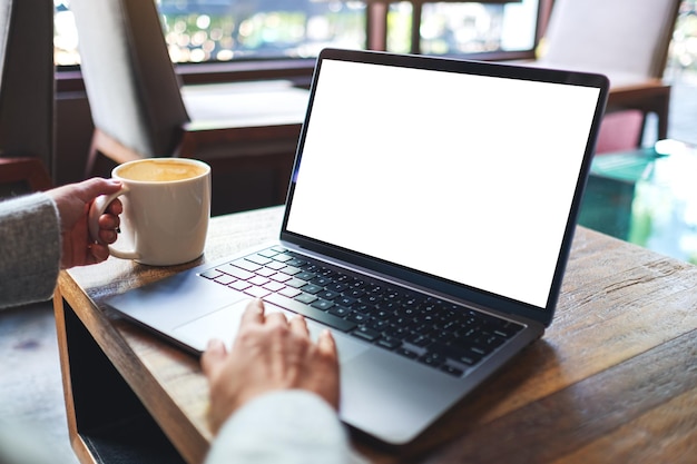 Imagem de maquete de uma mulher tocando no touchpad do computador portátil com tela branca em branco do desktop enquanto bebe café