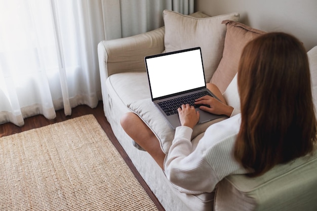Imagem de maquete de uma mulher trabalhando e digitando em um computador portátil com tela em branco no sofá em casa
