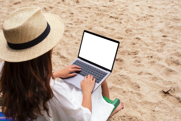 Imagem de maquete de uma mulher usando e digitando em um laptop com uma tela em branco enquanto está sentada em uma cadeira de praia