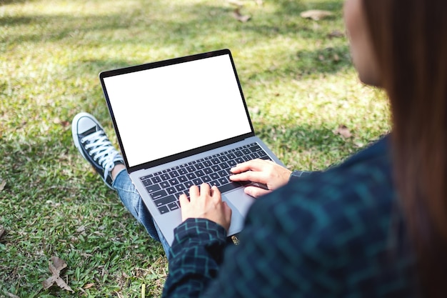 Imagem de maquete de uma mulher usando e digitando em um laptop com uma tela em branco, sentada ao ar livre com um plano de fundo da natureza