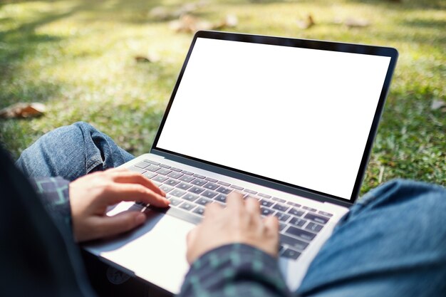 Imagem de maquete de uma mulher usando e digitando em um laptop com uma tela em branco, sentada ao ar livre com um plano de fundo da natureza