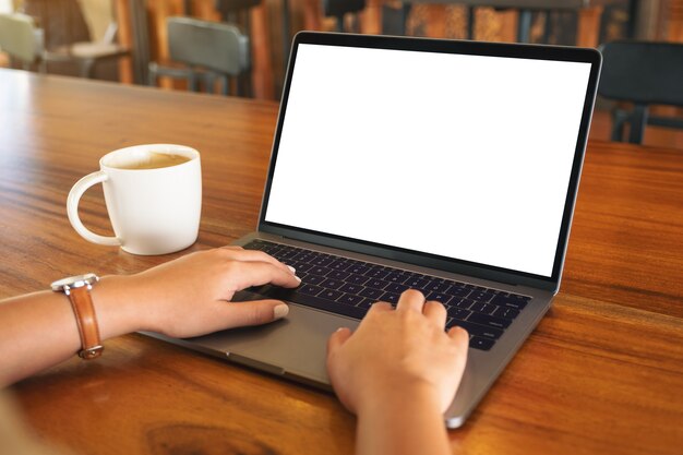 Imagem de maquete de uma mulher usando e digitando no laptop com uma tela em branco e uma xícara de café na mesa de madeira